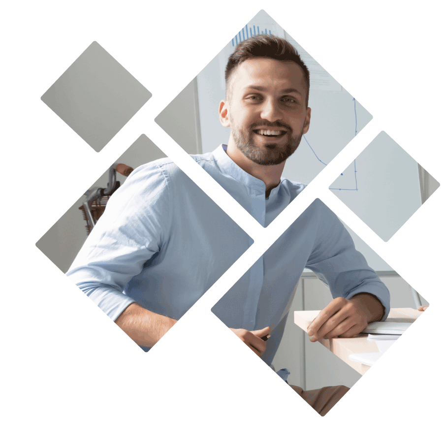 A man at a desk with a laptop, smiling at a framed picture of himself.