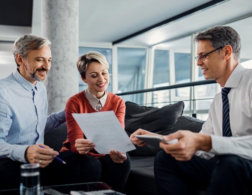 A trio of insurance individuals on a couch, engaged in discussion while examining paperwork.